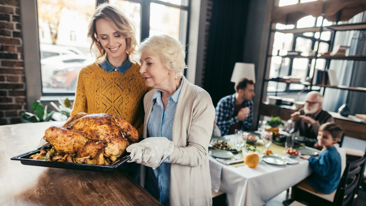 two women carrying tray with turkey to dinner table
