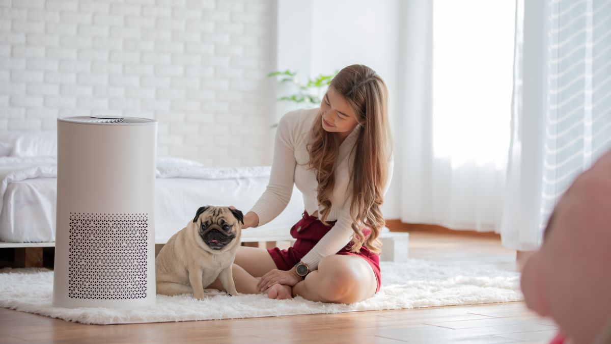 Woman petting dog on floor next to air purifier