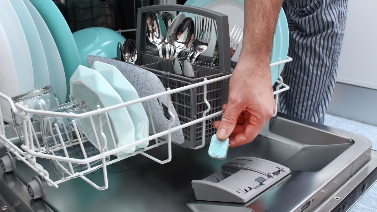 Man's hand puts dishwashing tablet into dishwasher