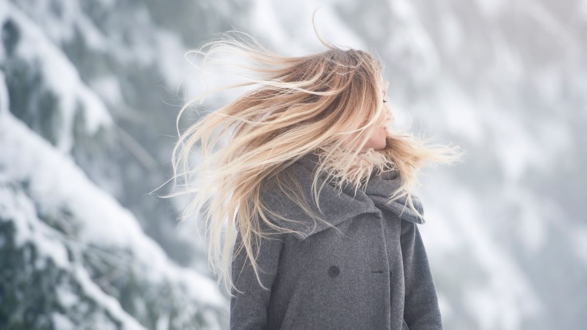 woman with long hair in front of snow-covered evergreens
