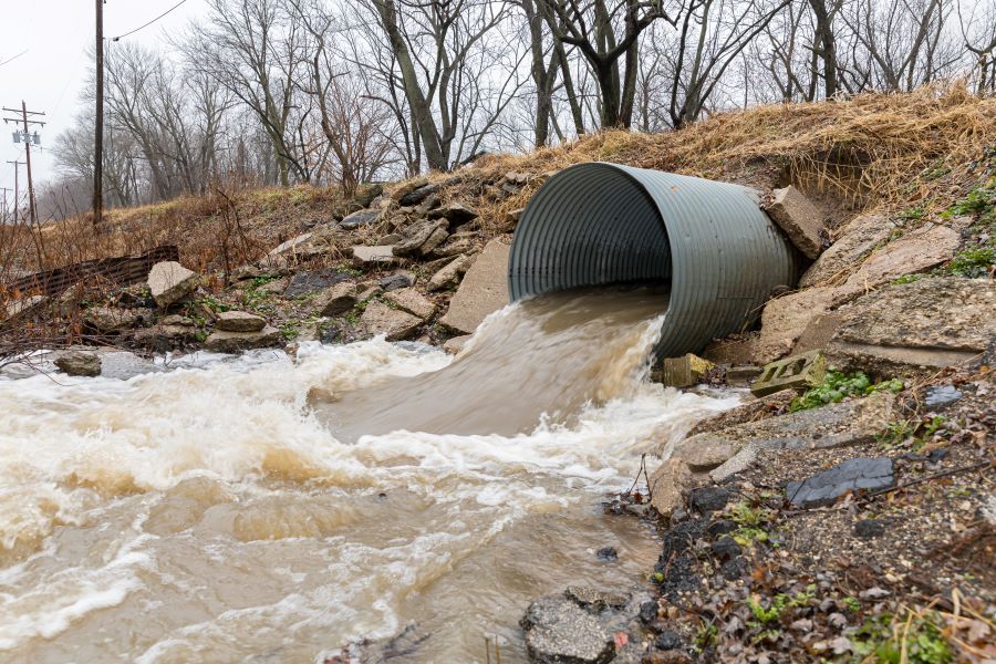 Stormwater runoff flowing through metal drainage culvert after heavy rain