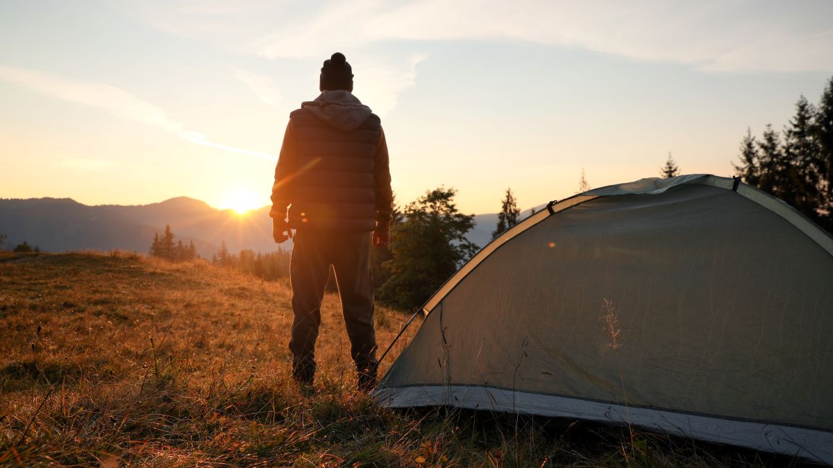 Man standing by tent watches sunset