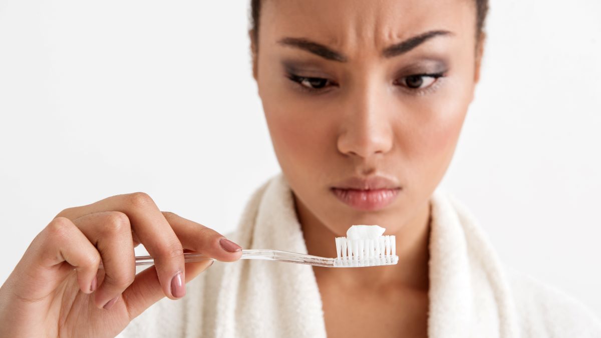 Woman looking at toothpaste on toothbrush with concern