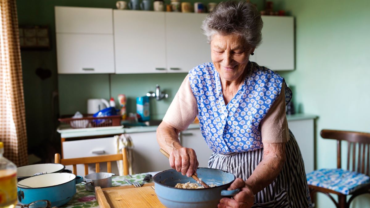 older woman wearing apron and mixing batter in the kitchen