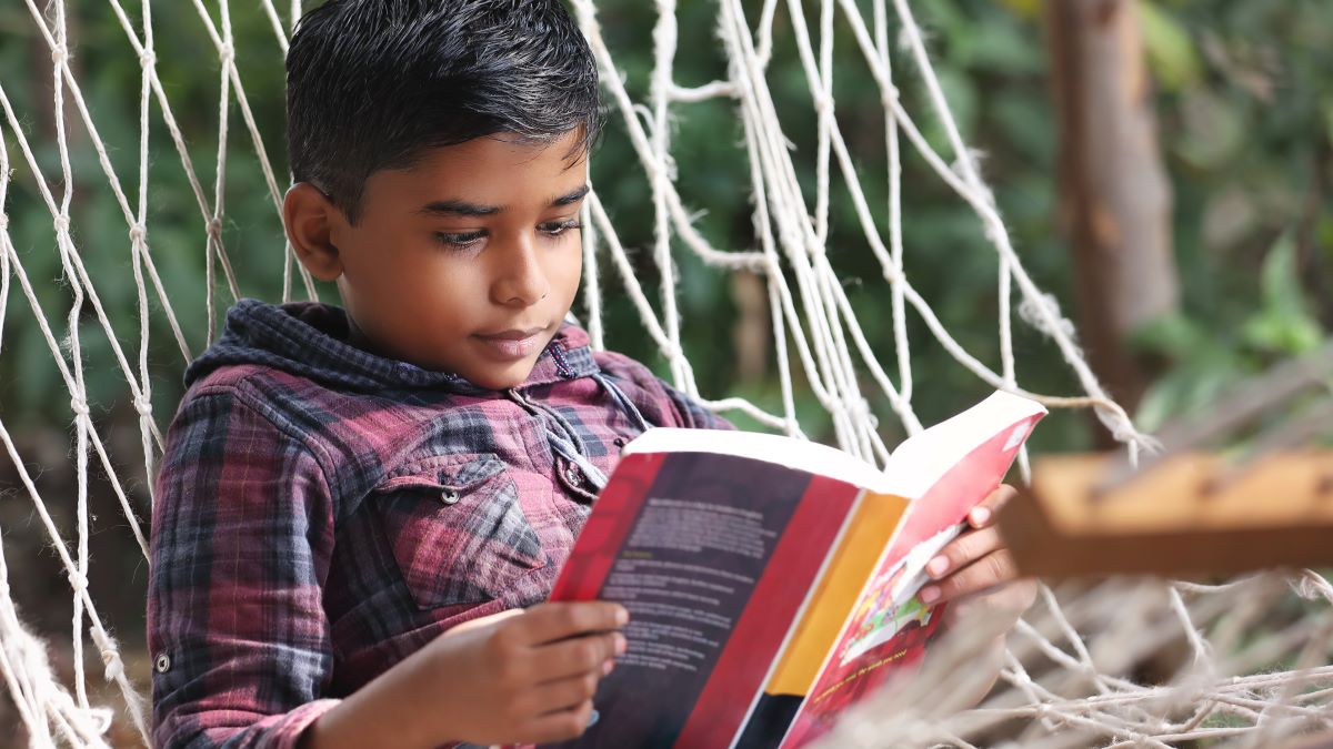 boy reading book on a hammock in the summer