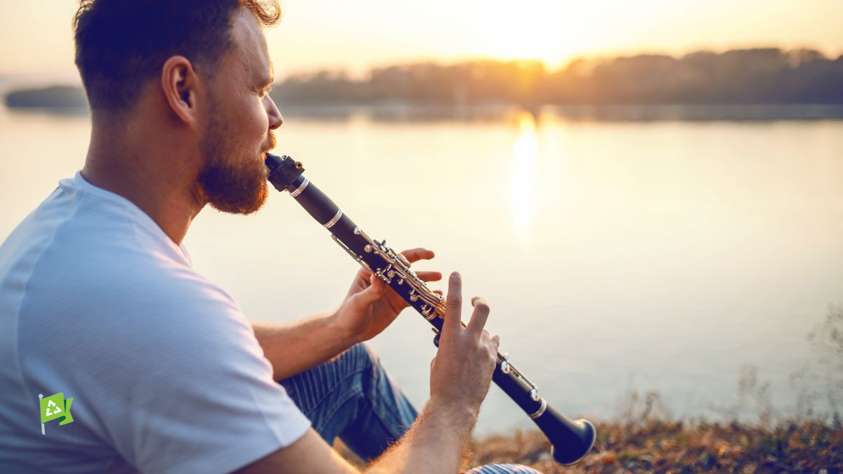 Man playing clarinet watching sun set over lake