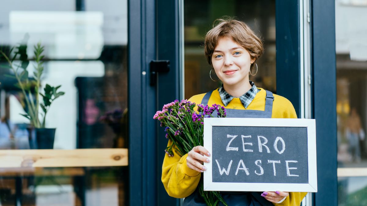 small business owner holding "zero waste" sign in front of her store