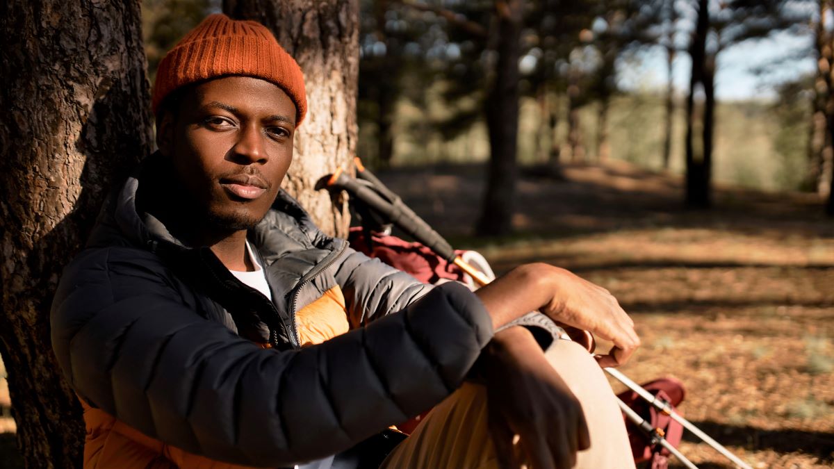 Young black man in outdoor gear leaning against tree